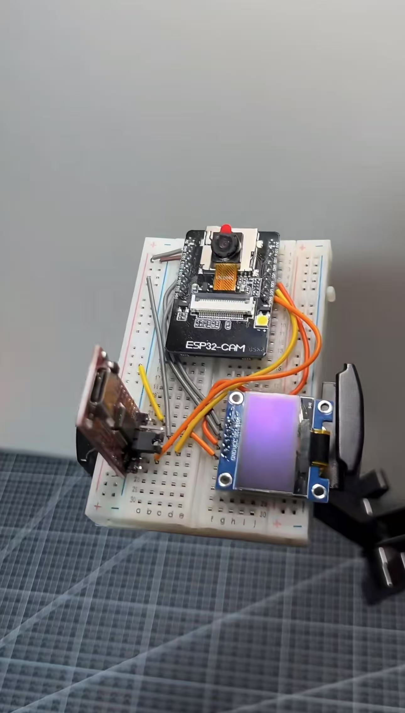 A breadboard setup featuring an ESP32-CAM module, a small display screen, connecting wires, and various electronic components arranged for a project.